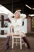 Model wearing the Valencia Two-Piece Set, a cropped cream embroidered bomber jacket and matching high-waisted shorts with tall boots